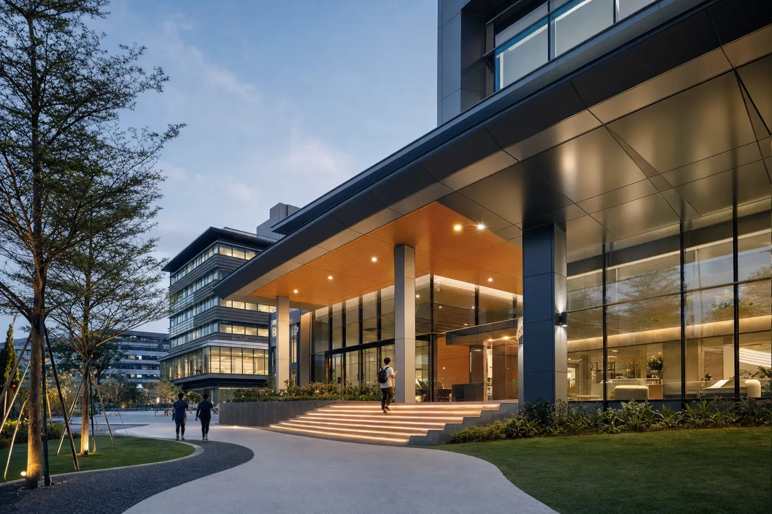 Campus building entrance at dusk with students walking up the lit steps