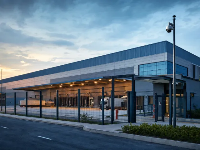 Fenced logistics warehouse with loading bays and a camera on a mast at the gate